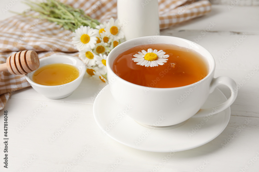 Composition with tasty chamomile tea, flowers and honey on light wooden background Composition with tasty chamomile tea, flowers and honey on light wooden background