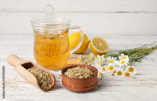 Composition with tasty chamomile tea, flowers and lemon on light wooden background