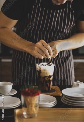Unrecognizable barista carefully decorating creamy foam of iced coffee by using toothpick to draw chocolate patterns onto it like spider net to make it look more attractive to be drunk.