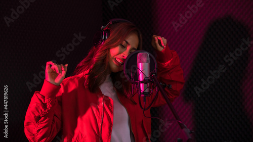 Ethnic female singer in headphones singing in microphone and recording music in studio