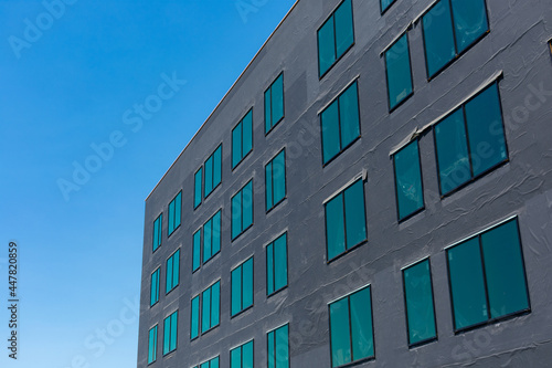 Exterior view of commercial building under construction. The wall is covered with black insulation material. Blue sky.