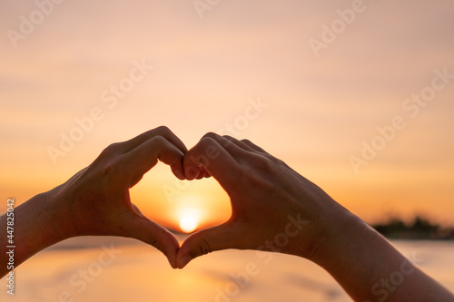 Woman hand do heart shape on sunset sky and bokeh.