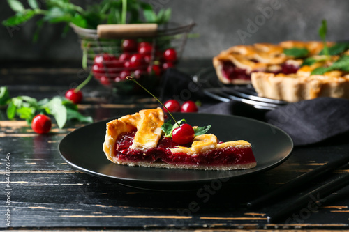 Plate with piece of tasty cherry pie on dark wooden table, closeup