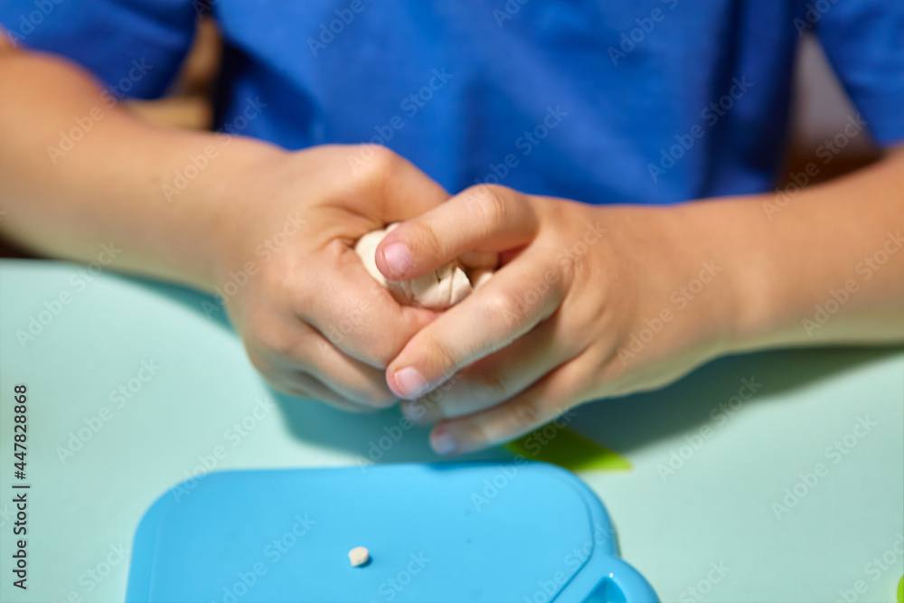 Child is sculpting with modeling clay. Art activity for children, indoor fun for kids concept. Close up and selective focus face and hands boy. Fun time for children activity at home or school.