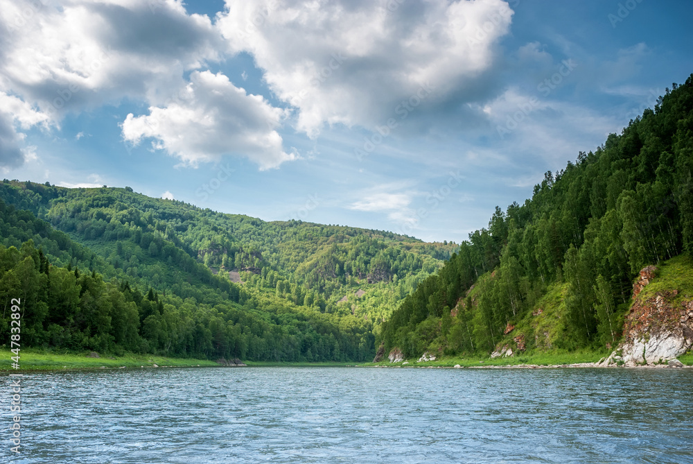 Landscape of Siberia. Kiya River, mountain banks and green forests in the Kemerovo region. Daytime landscape with blue skies and clouds.
