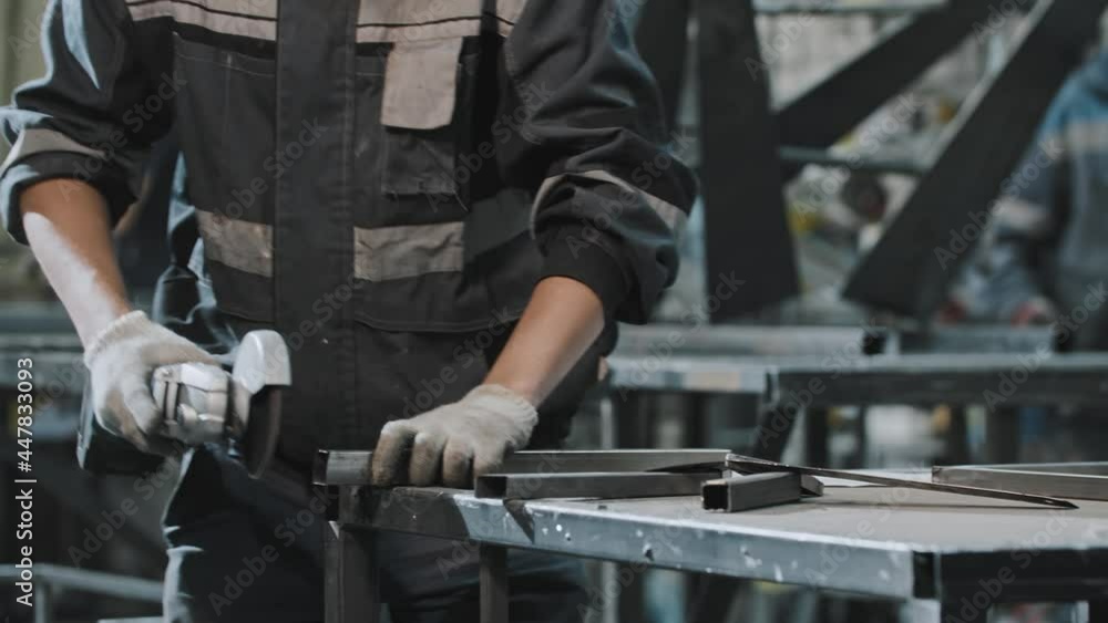 Young man in protective glasses working at the plant - grinding the cut on the metal detail Young man in protective glasses working at the plant - grinding the cut on the metal detail