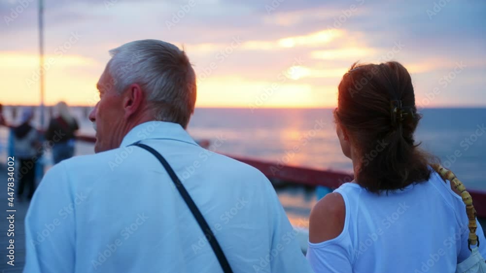 Senior Couple Walking Down The Baltic Sea Bridge In Palanga, Lithuania At Sunset - medium shot