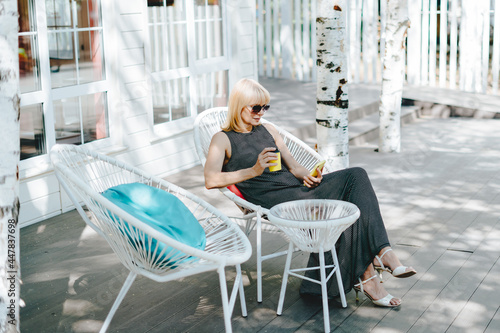 Mature adult woman having a video call chat with cellphone and drinking coffee. Happy senior outside in summer cafe. Using technology and texting online message at mobile phone.