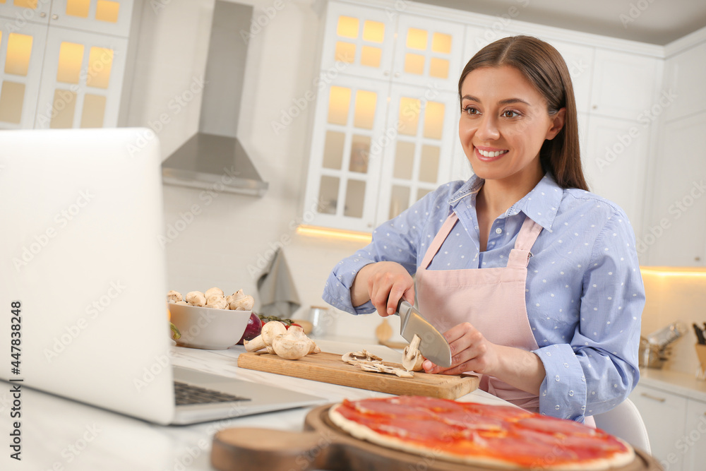 Happy woman cutting mushroom while watching online cooking course via laptop in kitchen Happy woman cutting mushroom while watching online cooking course via laptop in kitchen