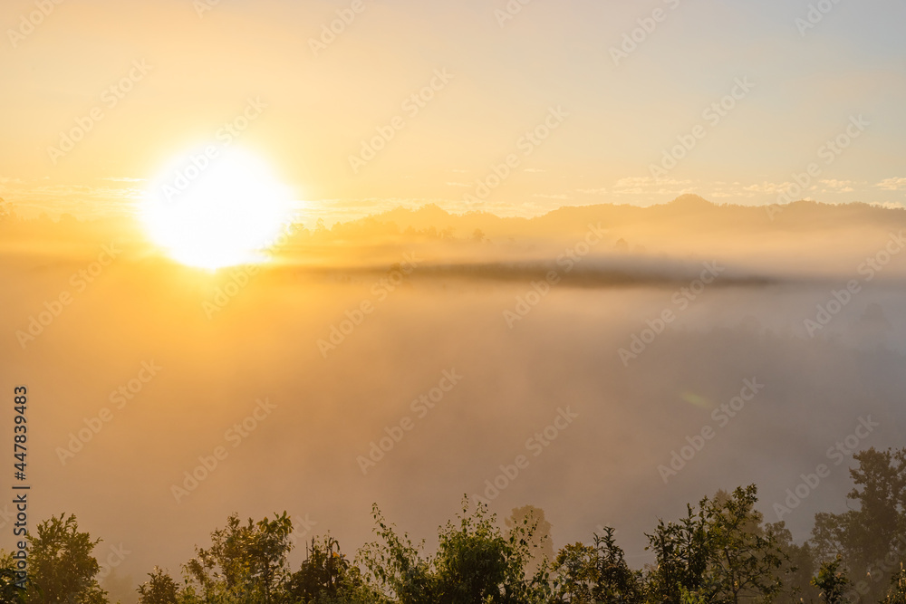 Sunrise in mountain mist with sun rays passing through a foggy hills
