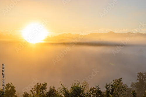 Sunrise in mountain mist with sun rays passing through a foggy hills
