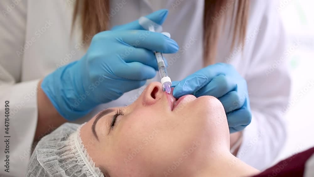Lip augmentation. Beautician injects hyaluronic acid into the lips of a girl with a syringe. The cosmetologist doctor performs the procedure in the cosmetology office. Plastic surgery. Lip augmentation. Beautician injects hyaluronic acid into the lips of a girl with a syringe. The cosmetologist doctor performs the procedure in the cosmetology office. Plastic surgery.