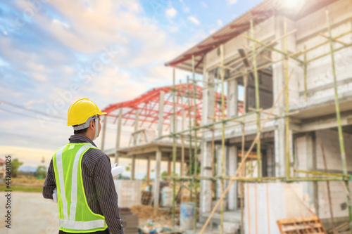 young professional engineer in protective helmet and blueprints paper at the house building construction site