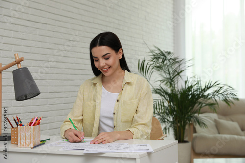 Young woman coloring antistress page at desk indoors