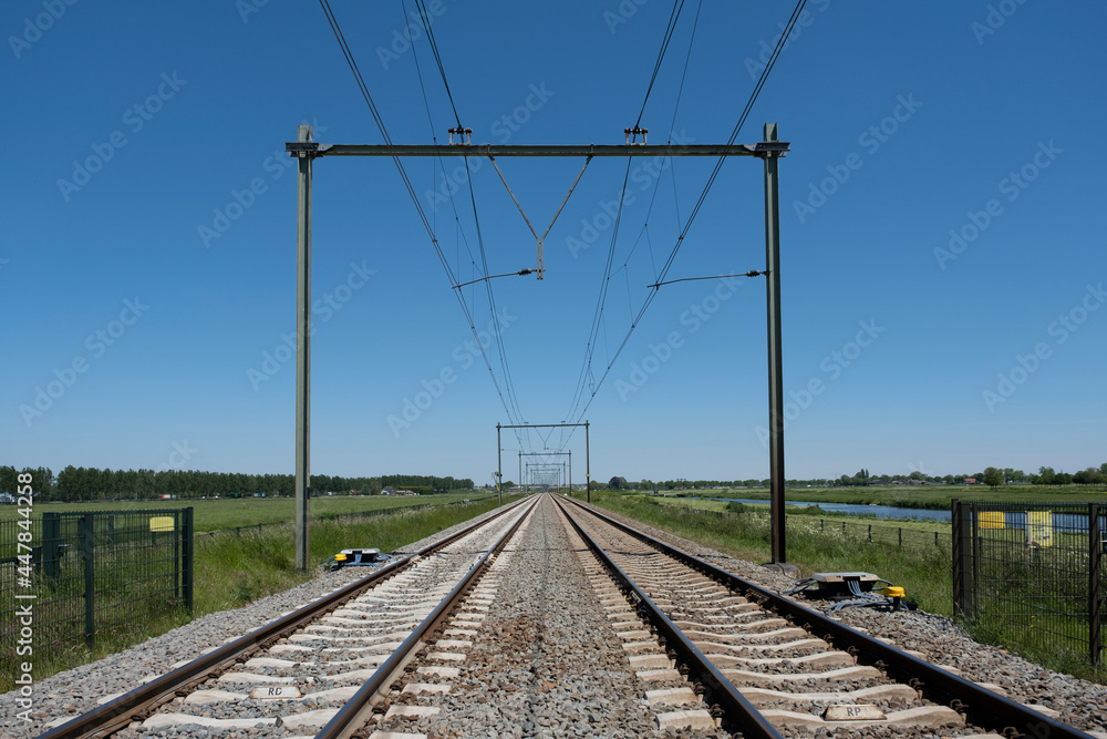 Two railway tracks with electric power cables and on the left side a train signal pole into the distance Two railway tracks with electric power cables and on the left side a train signal pole into the distance