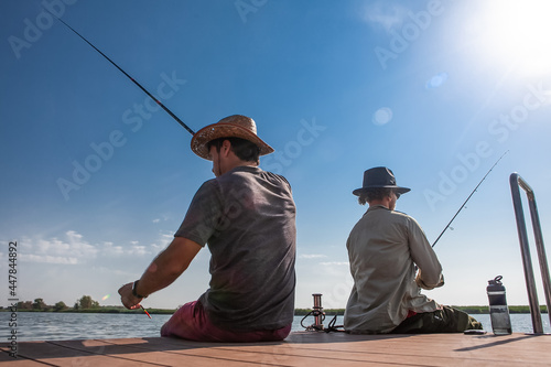two men on the pier are fishing with fishing rods in the summer