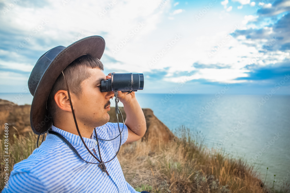 a man on a high hill at the sea looks through binoculars in the summer