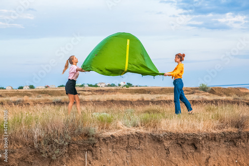 two women set up a tent in nature in summer