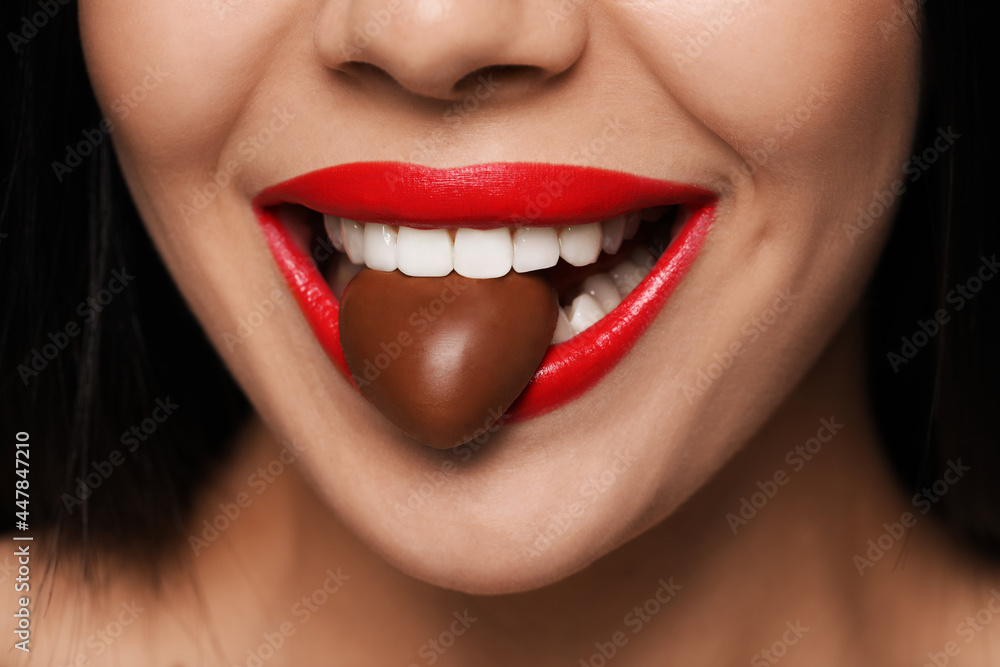 Young woman with red lips eating heart shaped chocolate candy, closeup Young woman with red lips eating heart shaped chocolate candy, closeup