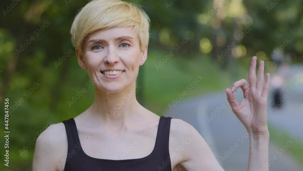 Portrait outdoors female athlete woman runner caucasian middle aged lady standing in park outdoor near green tree showing ok gesture okay sign symbol of satisfaction everything fine looking at camera Portrait outdoors female athlete woman runner caucasian middle aged lady standing in park outdoor near green tree showing ok gesture okay sign symbol of satisfaction everything fine looking at camera