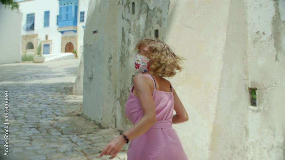 a tourist woman in a protective mask in the old city calls for her-follow me and runs ahead in her pink dress, in slow motion. a positive view of the new reality after the pandemic a tourist woman in a protective mask in the old city calls for her-follow me and runs ahead in her pink dress, in slow motion. a positive view of the new reality after the pandemic