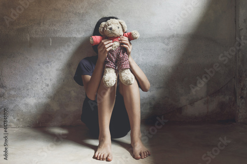 Child covered her face sitting alone on floor with her bear in dark room. concept for bullying, depression stress or frustration. photo