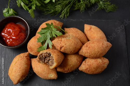 Deep fried kibbeh of ground beef meat mixed with bulgur, stuffed with fried minced meat with pine nuts on cutting board on dark background photo