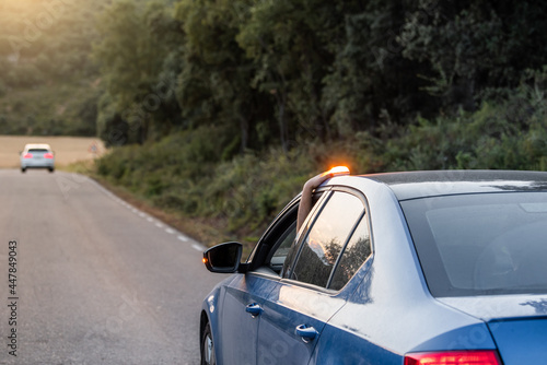 hand placing the new V16 emergency light, which replaces the emergency triangles, broken blue vehicle stopped on the road and with another car in the background