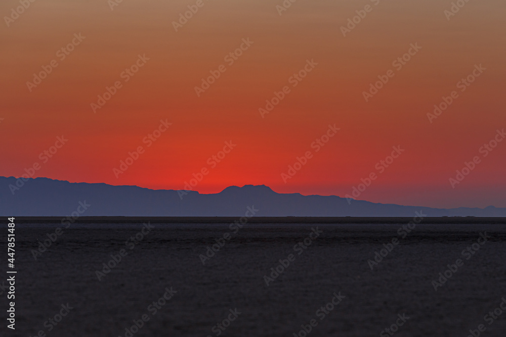 Scarlet sunrise on the large endorheic salt lake Chott el Djerid in the Sahara desert of southern Tunisia with the Atlas Mountains on the background