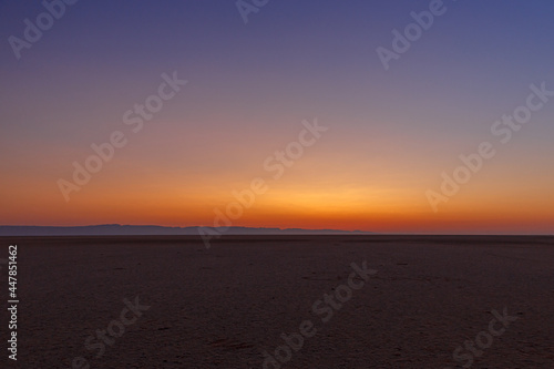 Orange sky before dawn on the large endorheic salt lake Chott el Djerid in the Sahara desert of southern Tunisia with the Atlas Mountains on the background