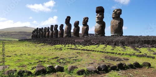 13 moai in Ahu Tongariki, Easter Island. Giant monoliths enclosed between a green lawn and the blue ocean behind them.