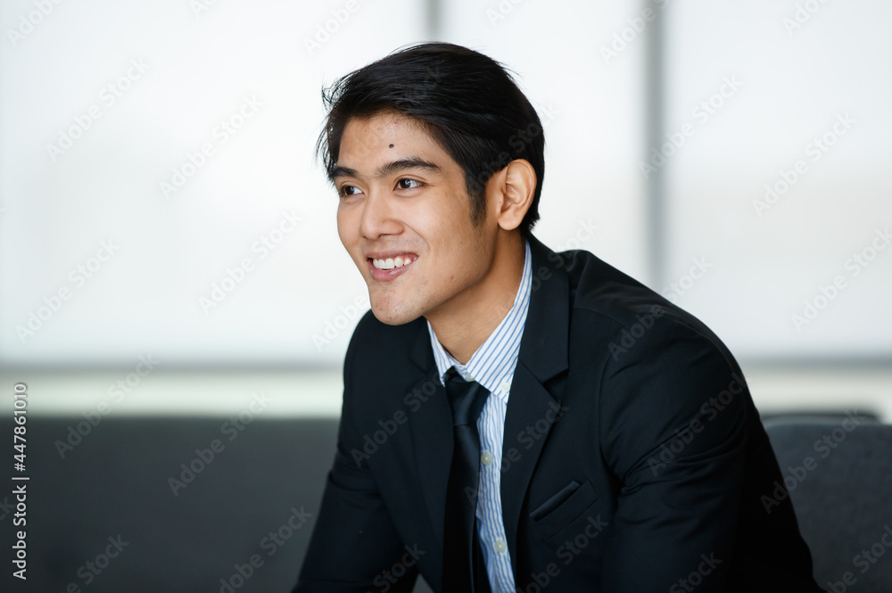 Portrait 20s handsome young successful Asian businessman wearing formal suit with necktie, smiling confidently and intelligently, sitting on comfortable sofa indoor office