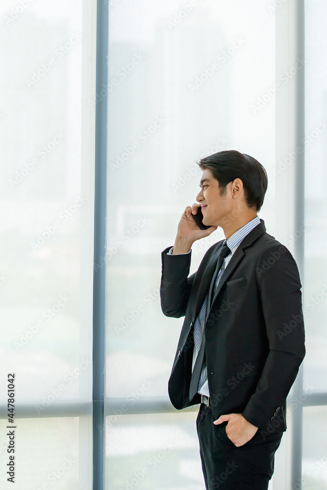 Closeup handsome young Asian businessman wearing formal suit, showing happy expression, smiling with confidence while talking mobile phone, presenting about technology and convenient communication. Closeup handsome young Asian businessman wearing formal suit, showing happy expression, smiling with confidence while talking mobile phone, presenting about technology and convenient communication.