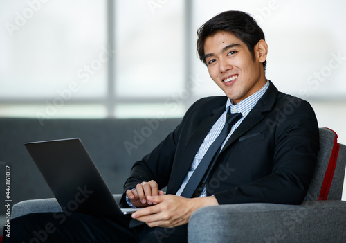 Portrait 20s handsome young successful Asian businessman wearing formal suit with necktie, smiling confidently and intelligently, sitting on comfortable sofa indoor office