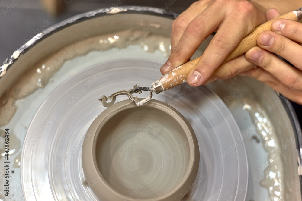 Fototapeta premium The hands of the master ceramist with a special tool align the almost finished cup on the potter's wheel