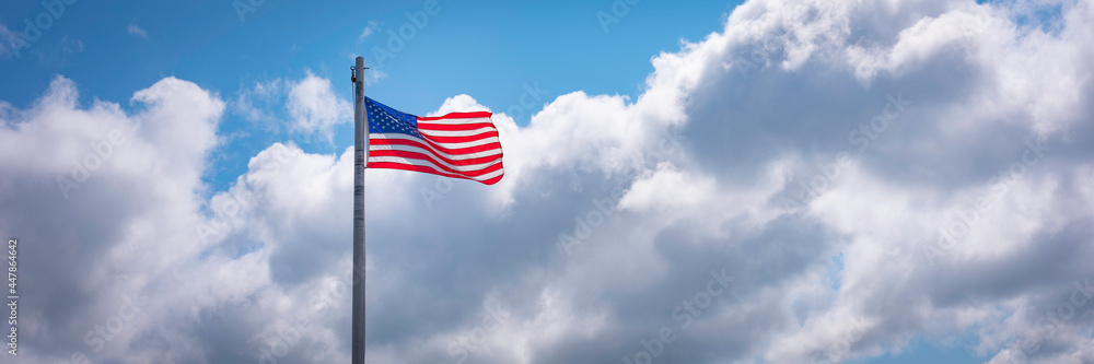 American Flag Waving in the Wind on White Clouds in the background. Blue Sky and Dramatic Clouds behind American Flag. Symbol of Unity and Leadership. American Flag Waving in the Wind on White Clouds in the background. Blue Sky and Dramatic Clouds behind American Flag. Symbol of Unity and Leadership.