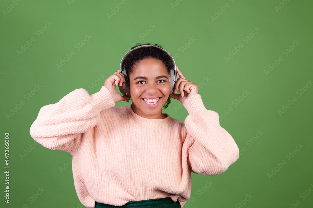 Beautiful african american woman on green background with wireless headphones huge smile listen music enjoying song Beautiful african american woman on green background with wireless headphones huge smile listen music enjoying song