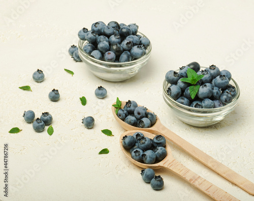 Fresh organic blueberries with leaves in bowl and spoon on grey background. 