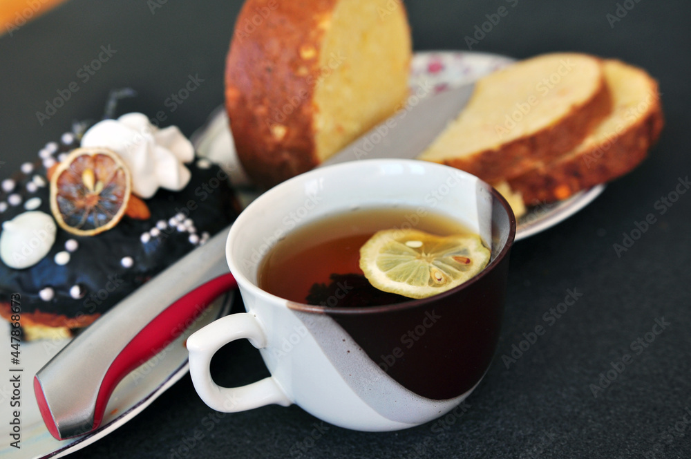 Cup of black tea with a slice of lemon and Easter buns on a plate Cup of black tea with a slice of lemon and Easter buns on a plate