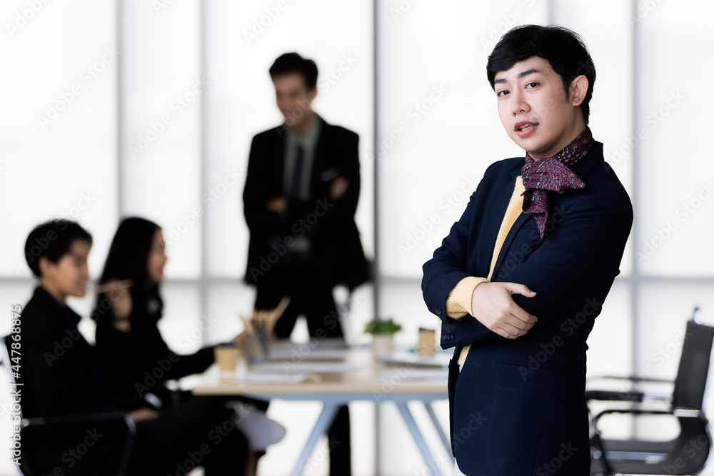 Portrait of LGBTQ transgender man office employee in casual suit standing and pose to camera with cheerful and happy gesture with team colleagues blur in background. Portrait of LGBTQ transgender man office employee in casual suit standing and pose to camera with cheerful and happy gesture with team colleagues blur in background.