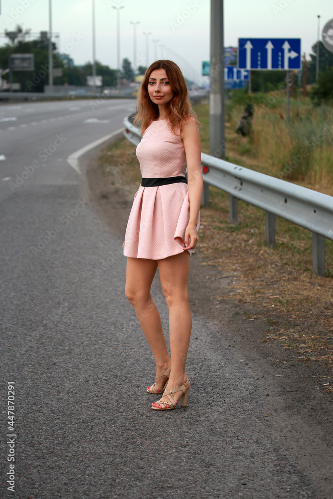 Alone beautiful woman in pink dress standing at the road
