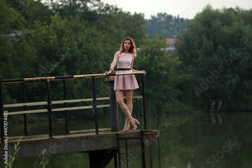 Portrait of beautiful woman in pink dress standing on a bridge at the lake