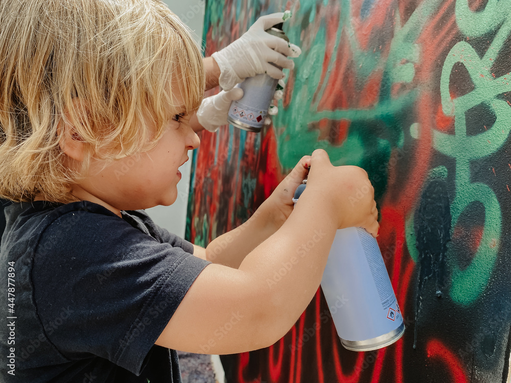 Fototapeta premium Caucasian three years old blonde child painting graffiti with a spray at the wall with effort face