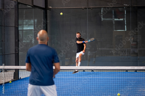 Monitor teaching padel class to man, his student - Trainer teaches boy how to play padel on indoor tennis court © damianobuffo