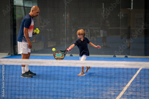 Monitor teaching padel class to child, his student - Trainer teaches little boy how to play padel on indoor tennis court