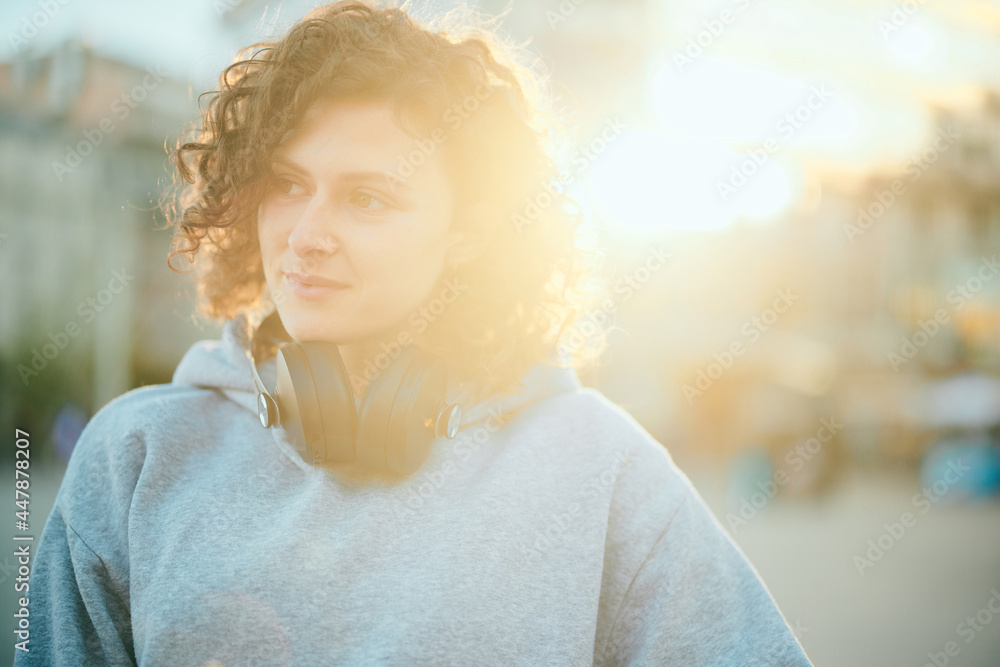 Portrait of a happy young woman standing on a street with headphones around her neck.