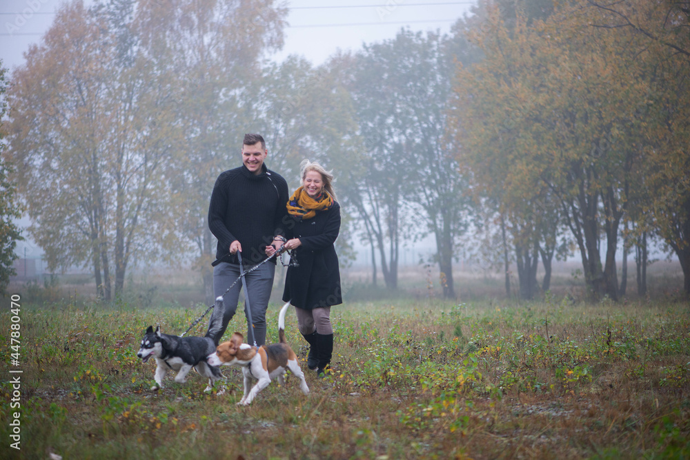 Happy young family couple with two dogs running in autumn park