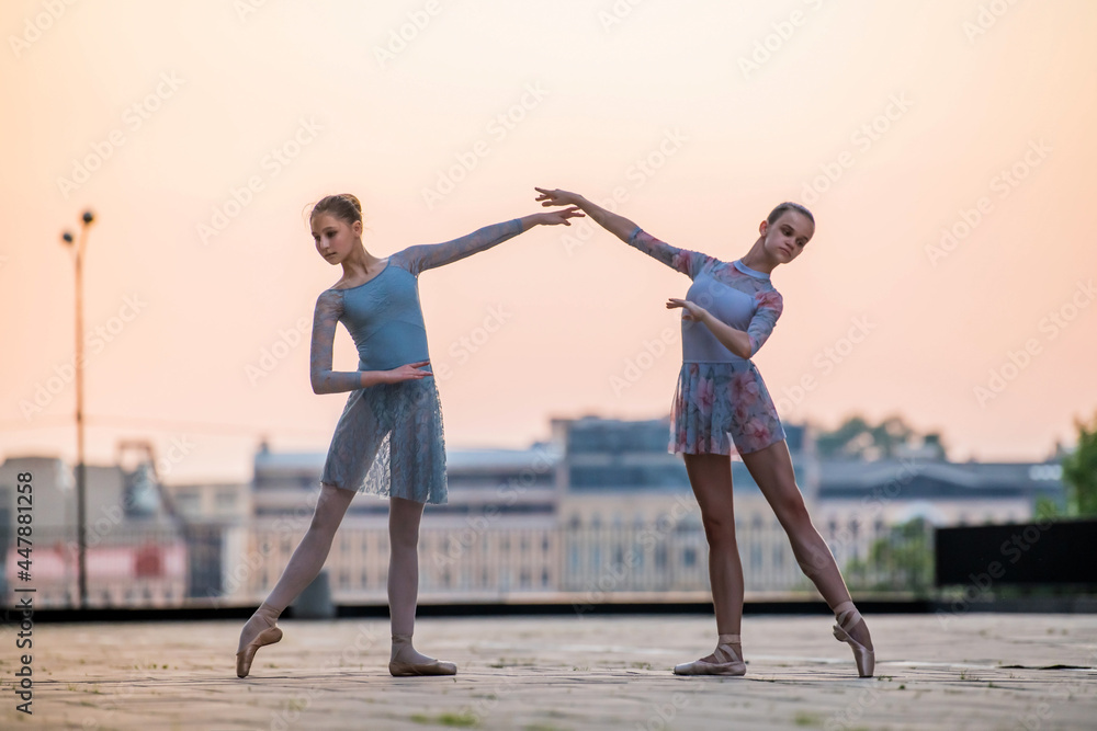 Fototapeta premium Two young ballerinas dancing in pointe shoes in city against the backdrop of sunset sky