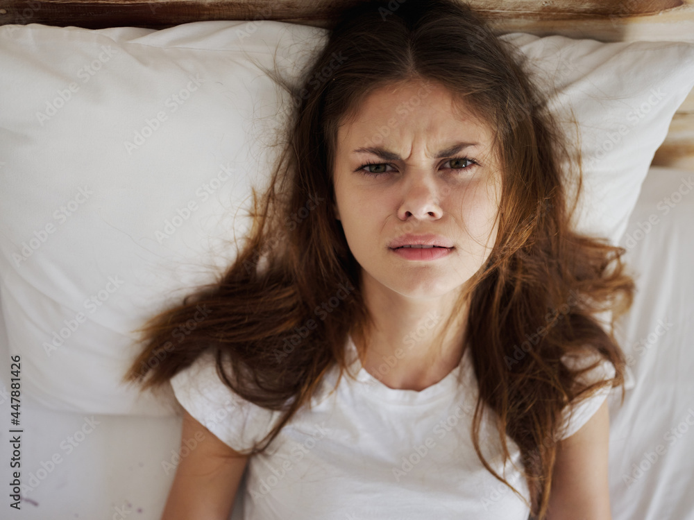 Angry woman lies in bed in a white t-shirt dissatisfied with a cold Angry woman lies in bed in a white t-shirt dissatisfied with a cold