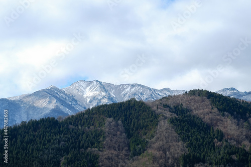 Beautiful snow mountain view with green forest and dry trees on blue clouds sky in morning time the view from shirakawago village Japan.